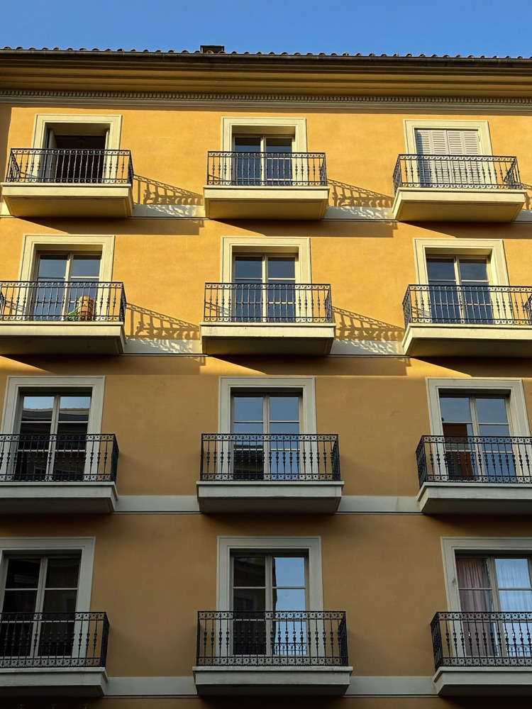 Ochre Spanish apartment facade with wrought-iron balconies in warm evening light